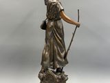 une statue antique en bronze représentant une femme tenant un bâton