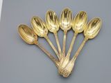 six gold spoons are arranged in a row on a gray surface