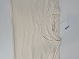 un t-shirt beige posé sur une table blanche, avec une étiquette dessus