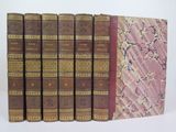 six old books are lined up in a row on a white surface
