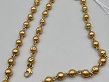 a gold beaded necklace with a tassel on a white background