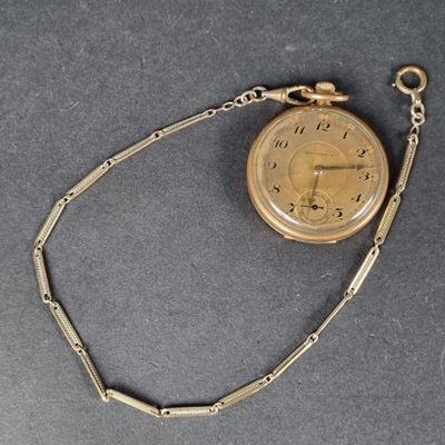 une montre de poche en or, suspendue à une chaîne, posée sur une table