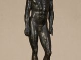 bronze statue of a man standing on a rock with his hands in his pockets