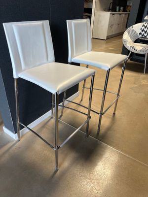 deux tabourets de bar en cuir blanc devant un mur noir