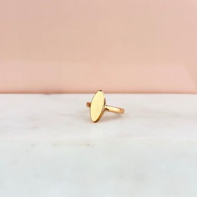 une bague en or ornée d'un petit motif ovale posé sur une surface en marbre blanc