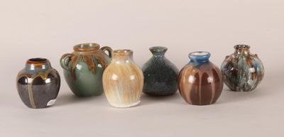 seven vases sitting in a row on a white surface