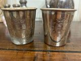 deux tasses en argent posées sur une table en bois, avec un vase en arrière-plan
