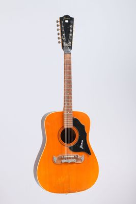 an orange acoustic guitar sitting on a stand against a white background