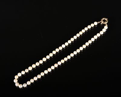 un collier de perles blanches avec un fermoir en or sur fond noir