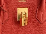 Le sac à main en cuir rouge est muni d'un fermoir doré sur la poignée.