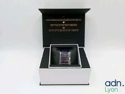 une boîte ouverte contenant une montre, posée sur une surface blanche