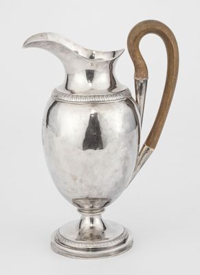 an antique silver pitcher with a wooden handle on a stand