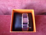 an orange box with a purple watch inside of it on a pink surface