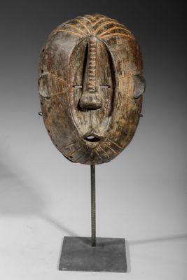 un masque en bois posé sur un socle métallique, sur fond blanc
