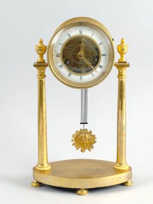 a gold clock with a pendulum on a stand