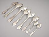 six silver spoons and a fork arranged in a row on a table