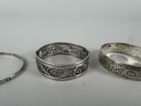 three silver bracelets with filigree designs on them on a white surface