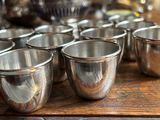 six silver cups sitting on a wooden table with a teapot in the background