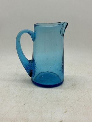 un pichet en verre bleu posé sur une table, sur fond blanc