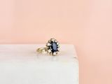 a blue sapphire and diamond cluster ring on a white marble block