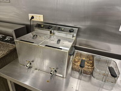 plan de travail en acier inoxydable équipé de deux friteuses et d'un panier rempli d'aliments