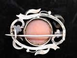 a close up of a silver broochle with a pink stone in it