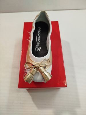 une chaussure blanche ornée d'un nœud doré, posée sur une boîte rouge