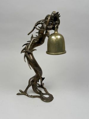 statue of a dragon holding a bell with a bell hanging from it ' s neck