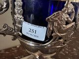 un trophée en argent posé sur une table, à côté d'un verre bleu