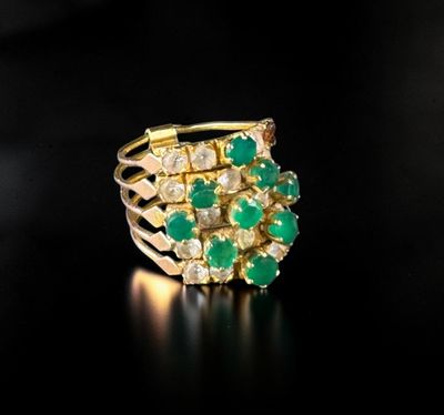 a close up of a gold ring with green stones on a black surface