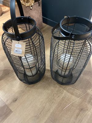 deux lanternes en métal noir posées sur un parquet, à côté d'une plante