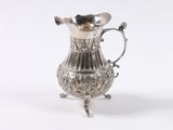 un pichet ancien plaqué argent posé sur un socle, sur fond blanc