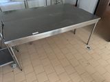 une table en acier inoxydable dans une cuisine, avec deux tabourets