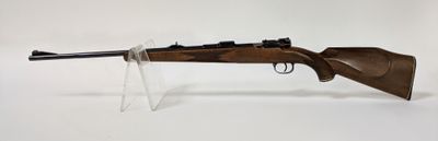 un fusil sur fond blanc, posé dans un support en verre transparent