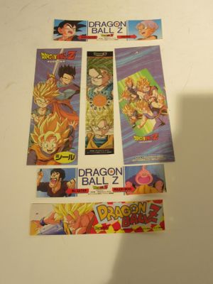 Plusieurs cartes Dragon Ball sont posées sur une table, sur laquelle se détache l'ombre d'une personne.