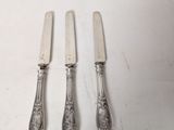 three forks and a knife on a table with a white table cloth