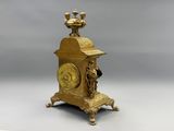 a gold clock sitting on a stand with a bird on top of it