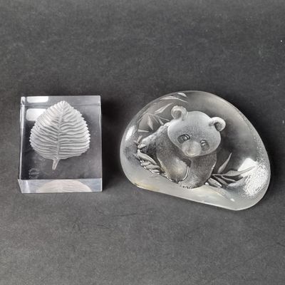 a glass object with a bear on it next to a leaf