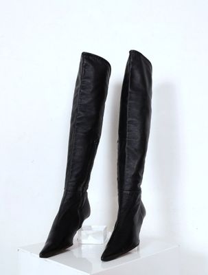 paire de bottes en cuir noir à hauteur du genou sur un piédestal blanc