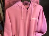 Un sweat à capuche rose et un pantalon de survêtement sont suspendus à un portant dans un magasin de vêtements