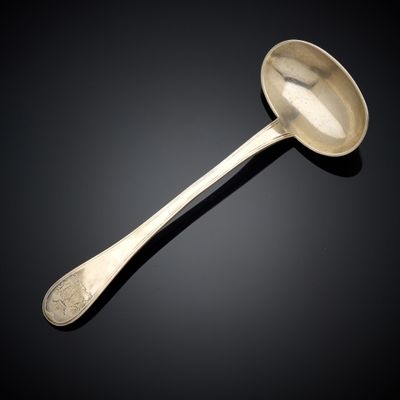 une cuillère ancienne en argent dont le manche repose sur une surface noire