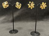 a pair of gold plated earrings on a black stand