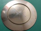 une assiette en argent ornée d'une croix sur un fond vert