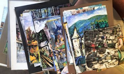 a person holding a bunch of paintings on a table