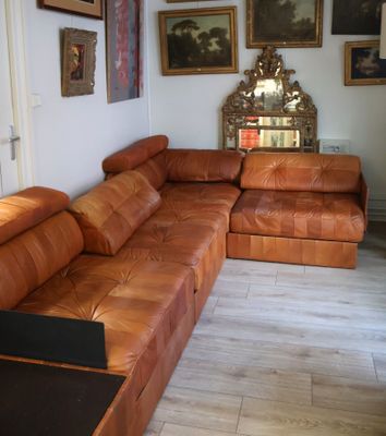 un canapé en cuir marron dans un salon où sont accrochés des tableaux au mur