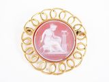 une image représentant une broche rose et dorée sur laquelle figure une femme assise sur un banc