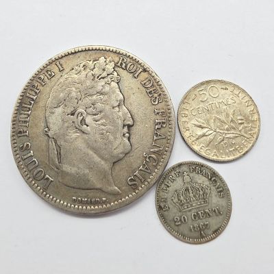 Trois pièces britanniques, une en argent et une en or, sont posées sur une surface blanche