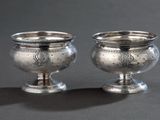 une paire de tasses argentées posées sur une surface grise avec un fond noir