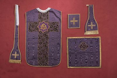 un gilet violet orné d'une croix, posé à côté d'autres objets sur une surface rouge