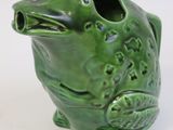a green frog shaped vase sitting on a white surface